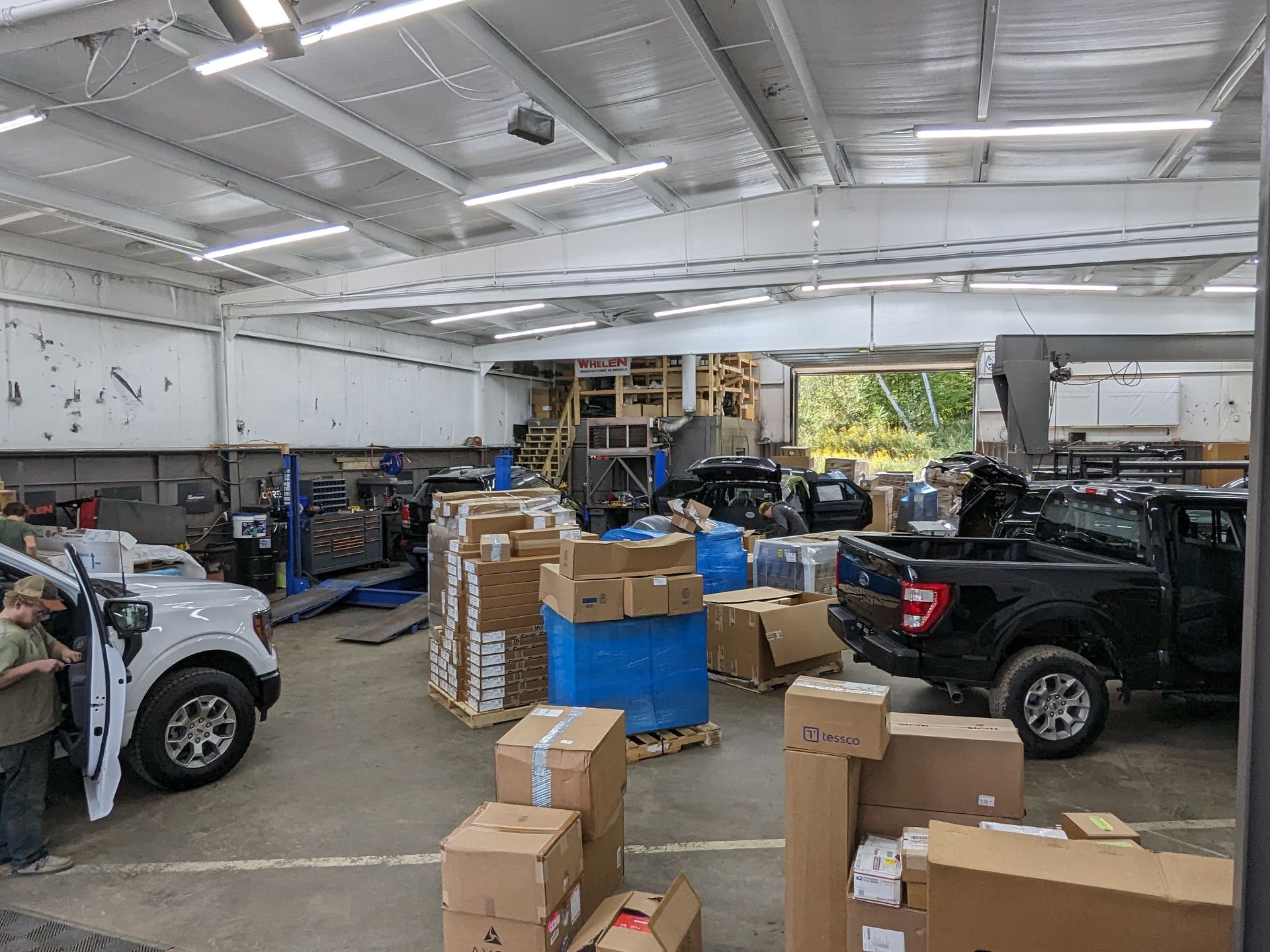 Shop interior with vehicles on lifts, parts boxes and supply drums