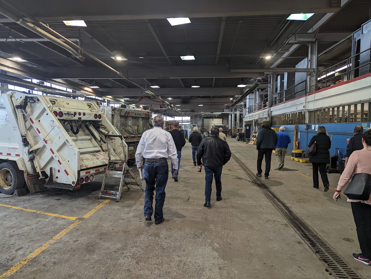 Large municipal maintenance garage with refuse trucks and staff walking the aisle