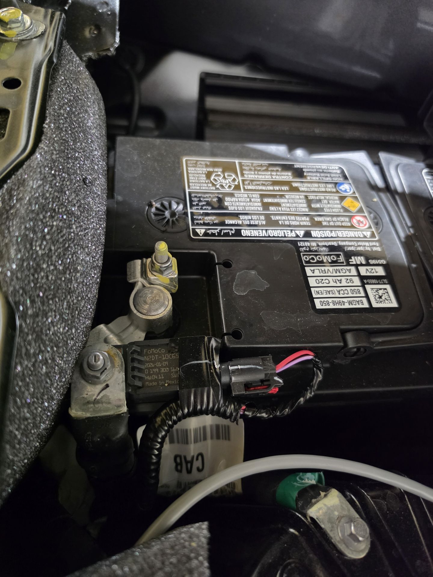 Engine bay of a vehicle with the battery, wiring and hood insulation visible