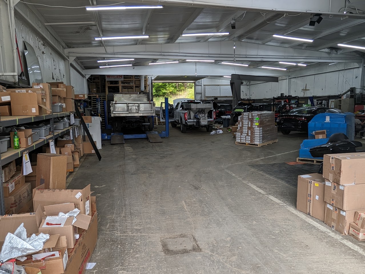 Upfit shop aisle with vehicles on lifts, benches and stacked parts boxes