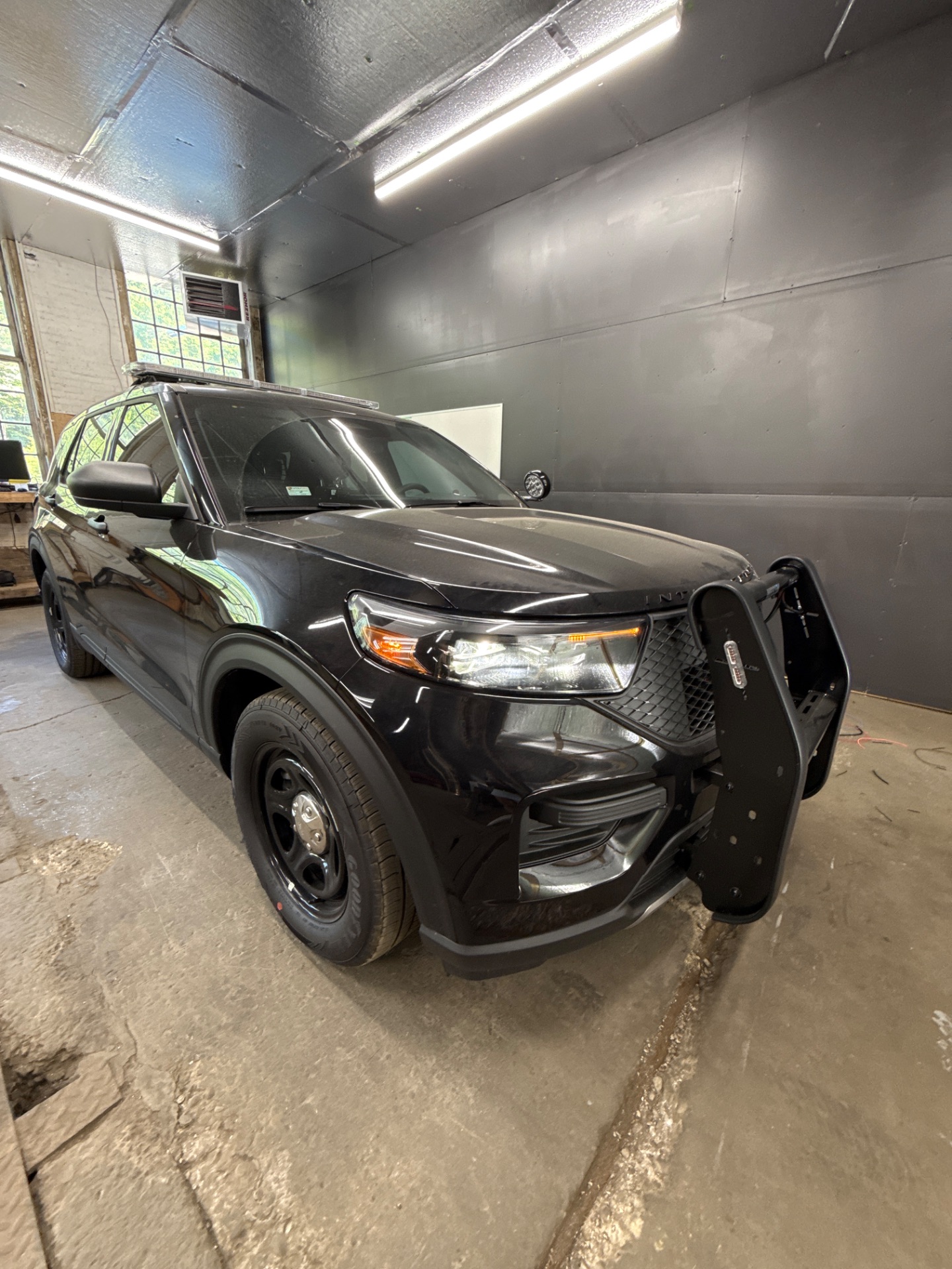 Black Ford Explorer police SUV with push bumper, front three-quarter in a shop bay